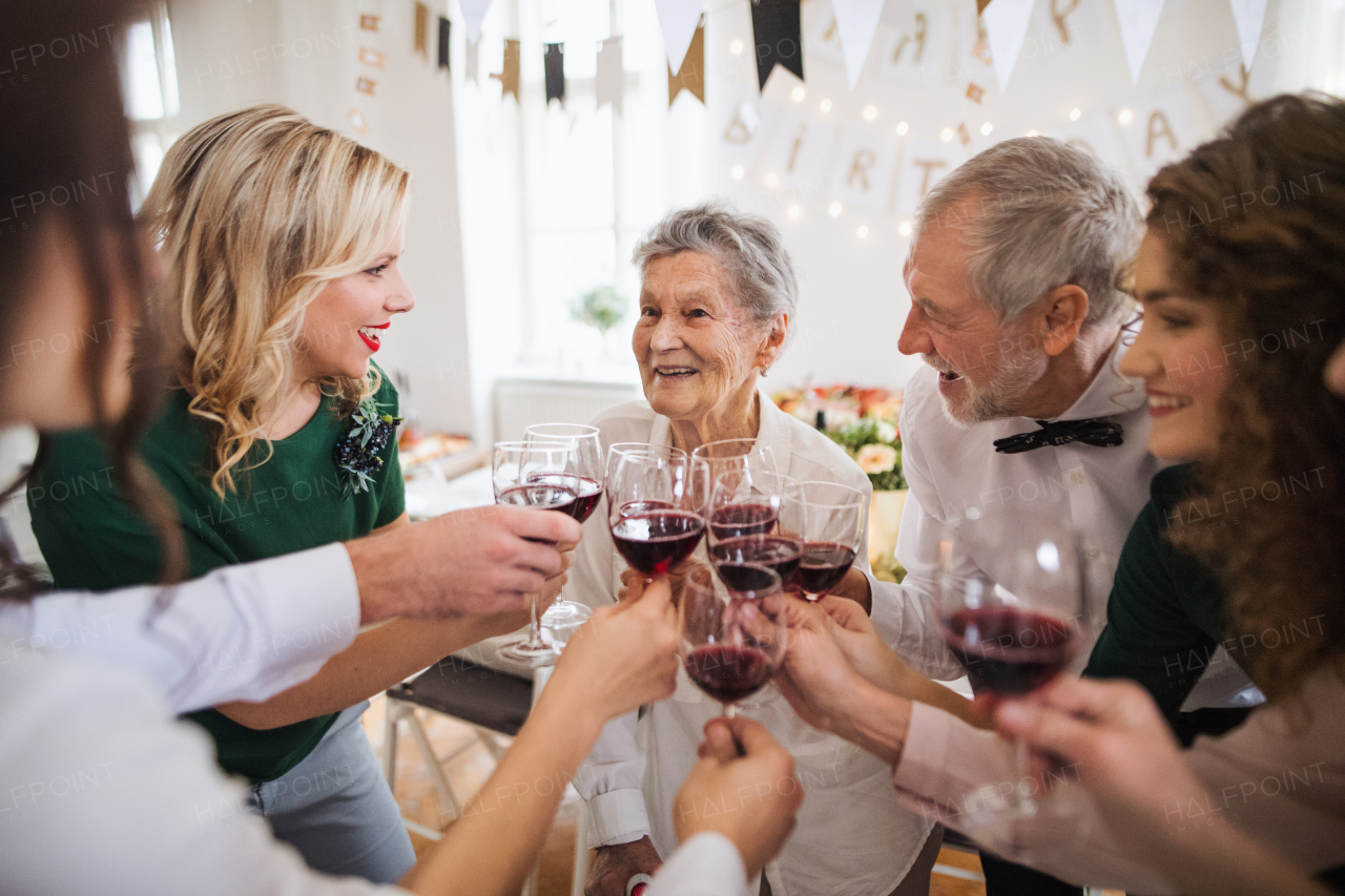 A multigeneration family clinking glasses with red wine on a indoor family birthday party, making a toast.