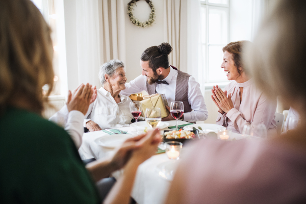 An elderly grandmother celebrating birthday with family and recieving a gift box, a party concept.