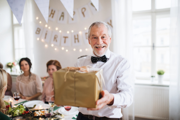 A senior man holding a present in a box on a indoor family birthday party, a celebration concept.