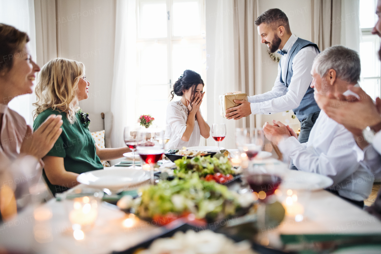 A man giving gift box to a young surprised woman on a family birthday or anniversary party.