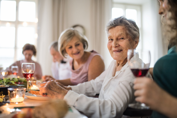 An elderly women with a family sitting at a table on a indoor family birthday party, eating.