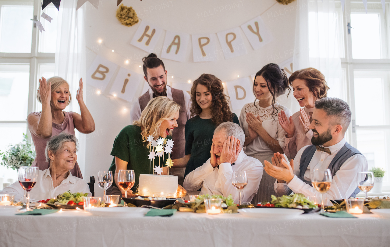 A senior man with multigeneration family and a cake celebrating birthday on an indoor party.