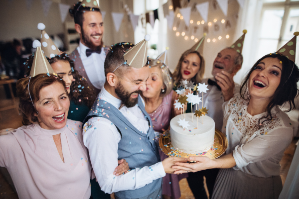 A portrait of multigeneration family with a cake and party hats on a indoor birthday party.