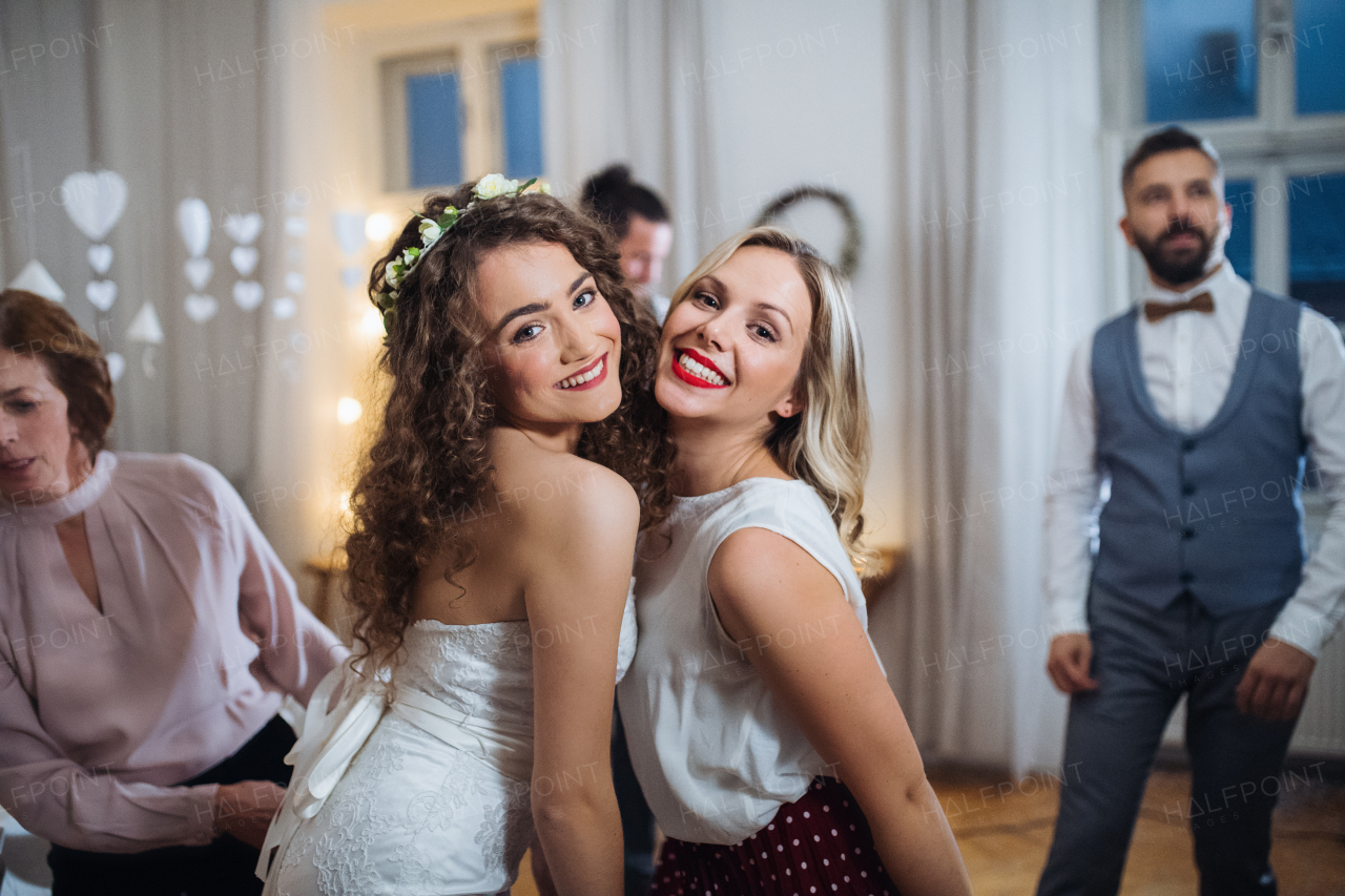 A portrait of young bride and her female friend or sister posing for a photograph on a wedding reception when dancing.