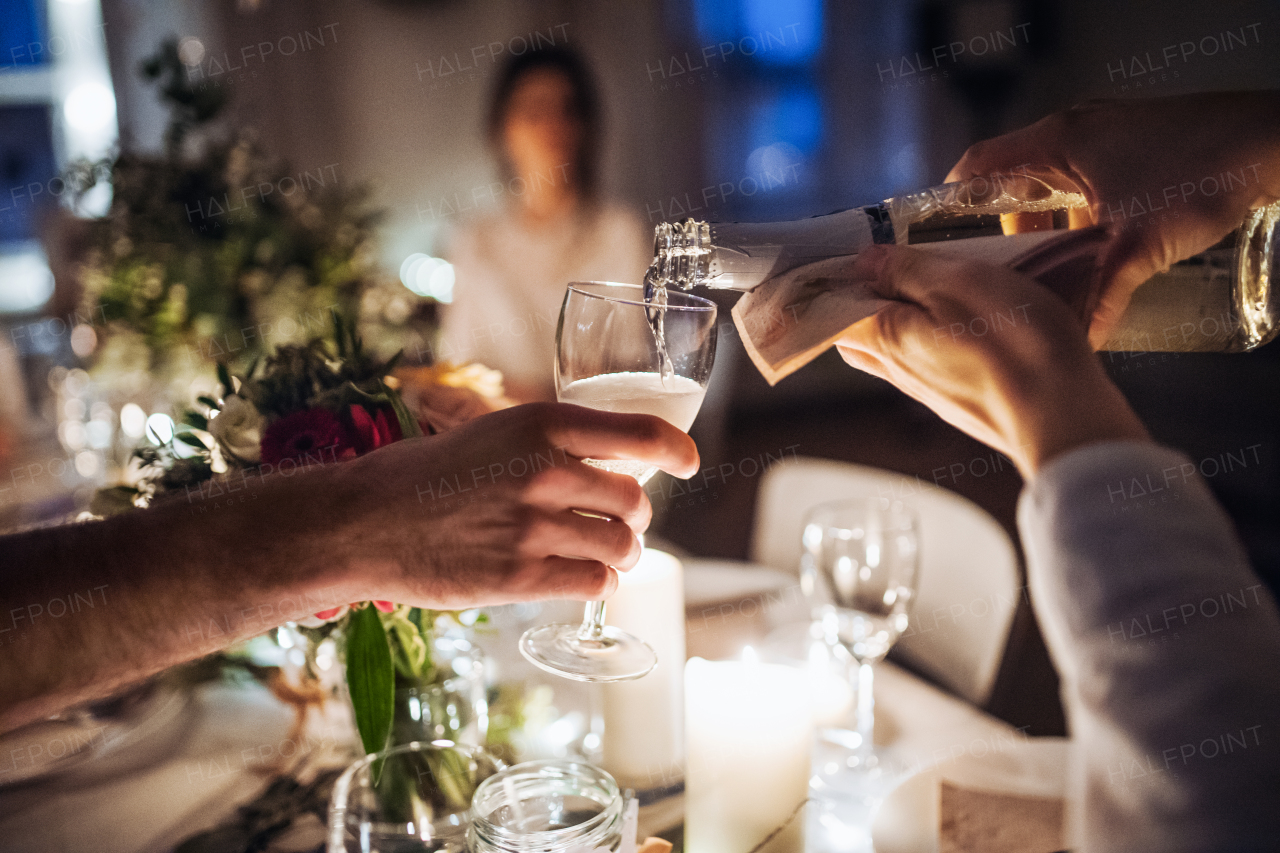 A midsection of unrecogniazble waiter pouring champagne into a glass on an indoor party at night.