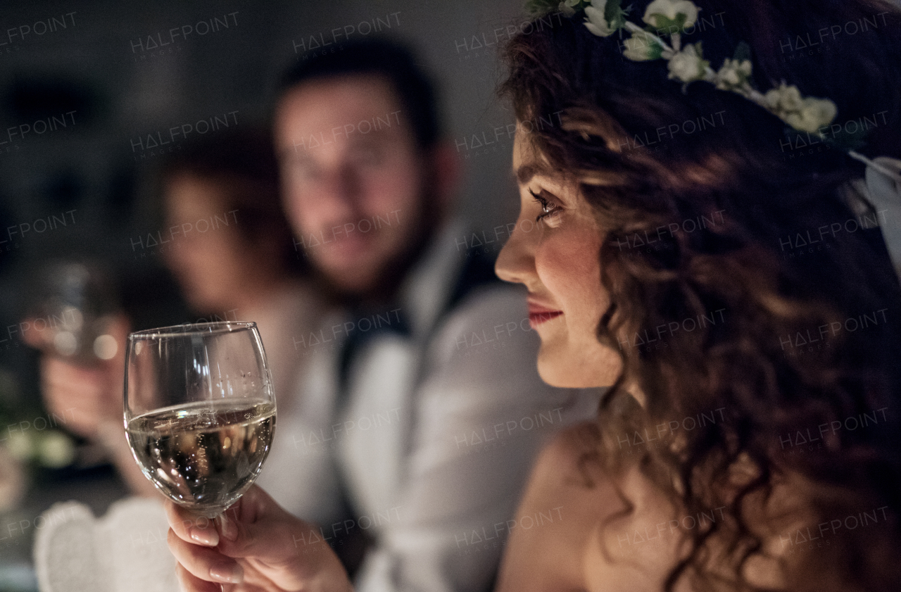 A close-up of a young bride sitting at a table on a wedding, holding a glass of white wine.