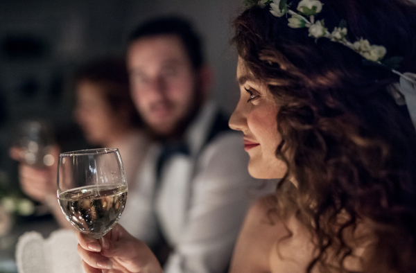 A close-up of a young bride sitting at a table on a wedding, holding a glass of white wine.