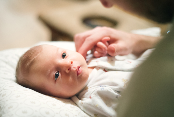 Cute newborn baby lying on bed, unrecognizable father stroking her head.