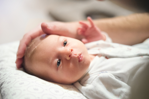 Cute newborn baby lying on bed, unrecognizable father stroking her head.