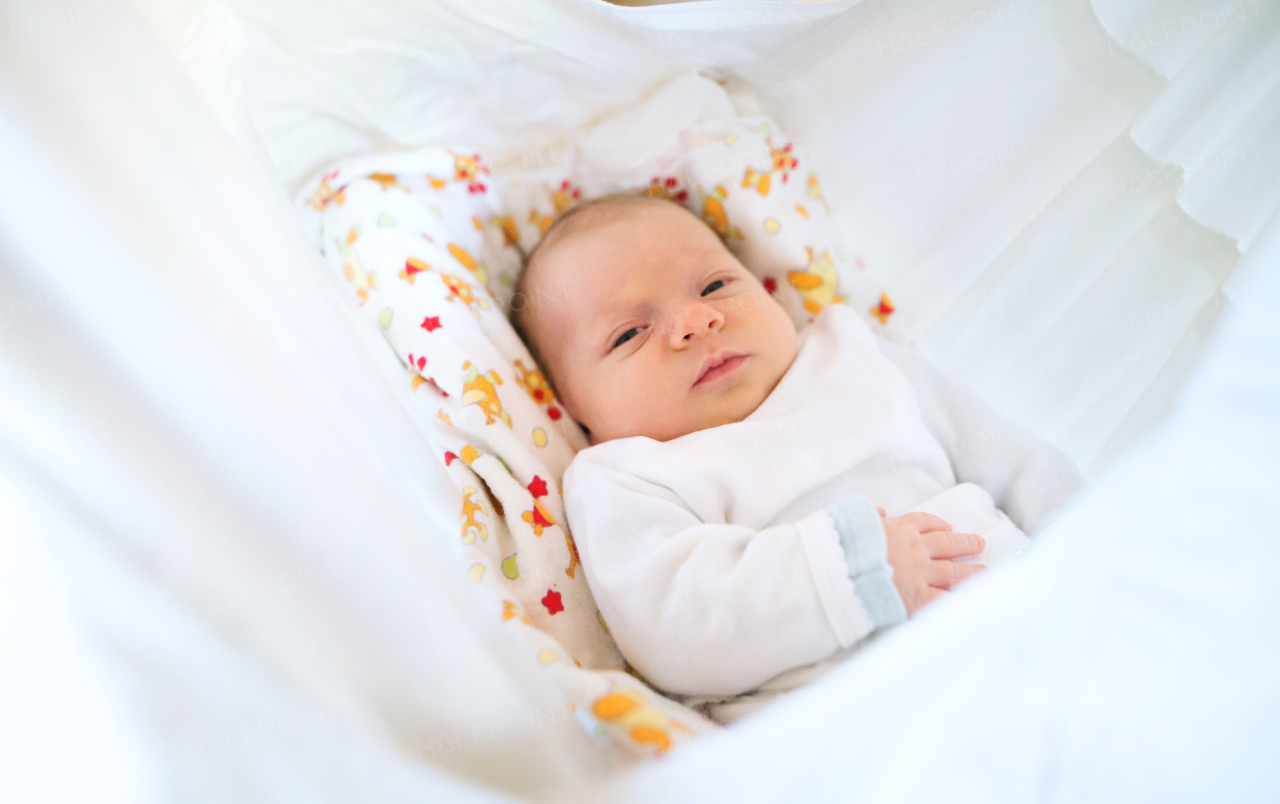 A close-up of a cute newborn baby lying on bed, covered by a white blanket.