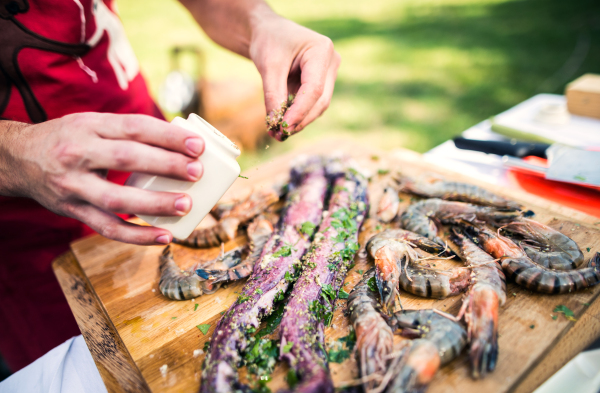 Unrecognizable man preparing seafood for a barbecue grill in the backyard on a sunny day. Close up.