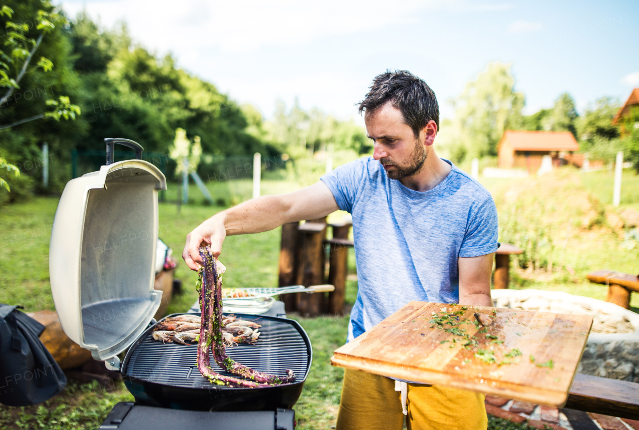 Mature man cooking seafood on a barbecue grill in the backyard on a sunny day.