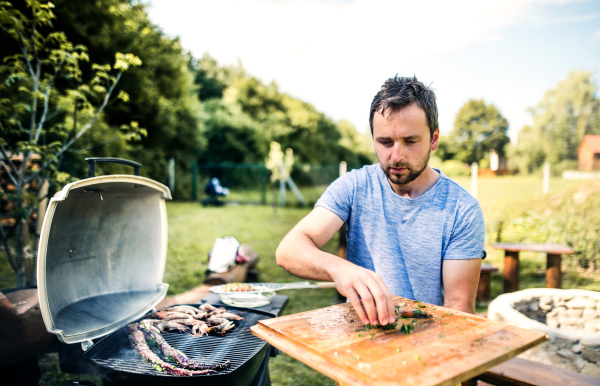 Mature man cooking seafood on a barbecue grill in the backyard on a sunny day.