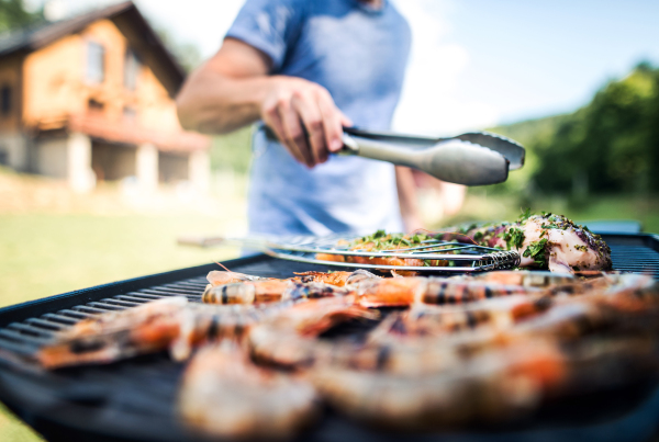 Unrecognizable man cooking seafood on a barbecue grill in the backyard on a sunny day.