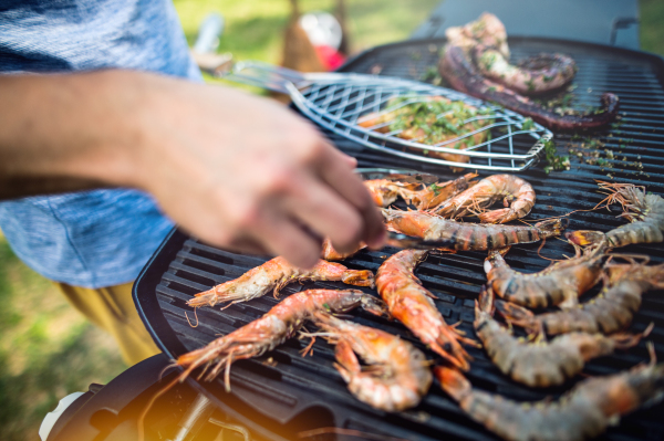 Unrecognizable man cooking seafood on a barbecue grill in the backyard on a sunny day. Close up.