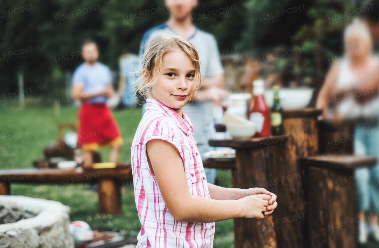 A happy small girl standing outdoors on a barbecue grill party in the backyard.