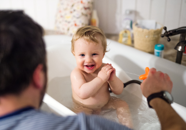 Unrecognizable father playing with a toddler boy in the bath in the bathroom at home. Paternity leave.