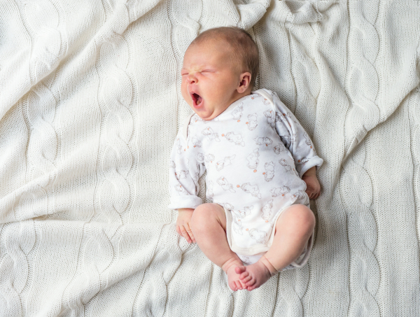 Cute tired newborn baby lying on a white blanket, yawning. Top view.