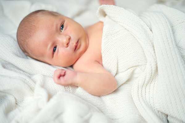 A close-up of a cute newborn baby lying on bed, covered by a white blanket.