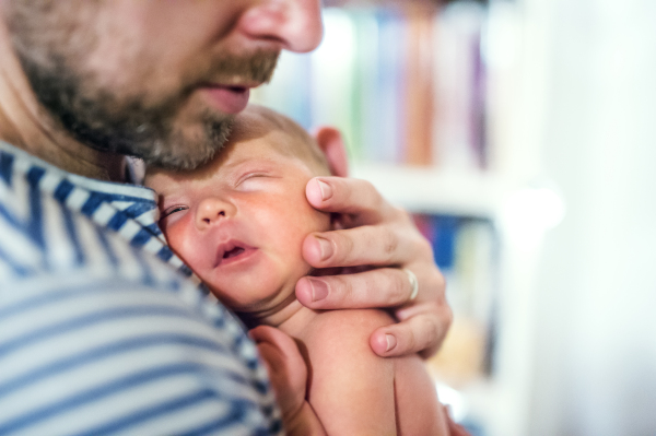 Unrecognizable father holding a newborn baby at home. Copy space.