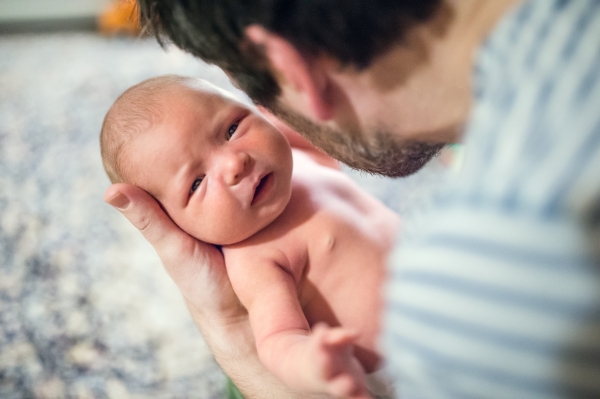 Unrecognizable father holding a newborn baby at home. Copy space.