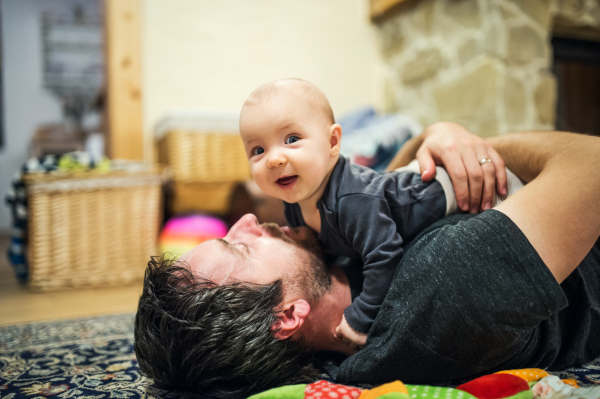 Father lying down on the floor with a baby girl at home. Paternity leave.