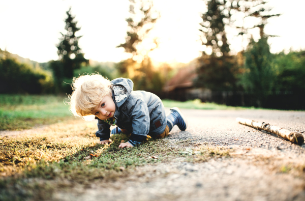 A happy little toddler boy crawling outdoors on a road at sunset.