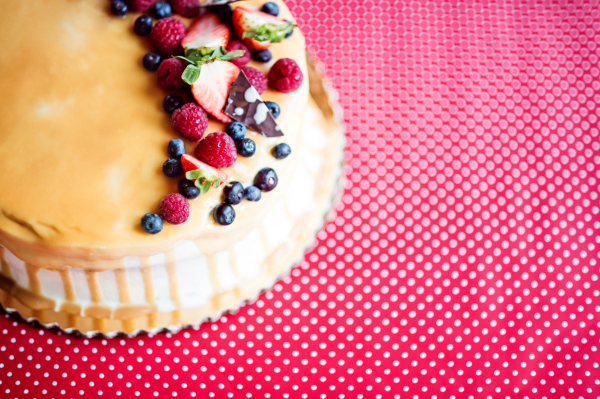 A birthday cake on a glass stand on the table, fruit on top. Red background. Top view. Copy space.