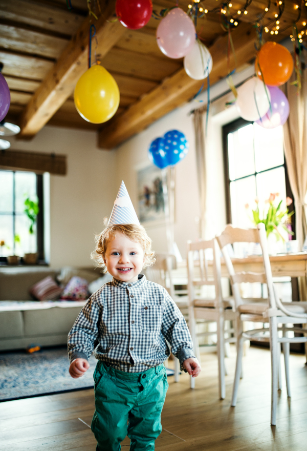 A happy toddler boy with a party hat walking inside at home.