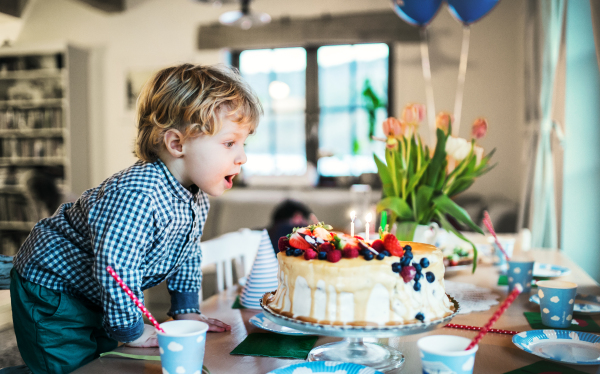 A boy standing on a chair, blowing out candles on a birthday cake. A birthday party.