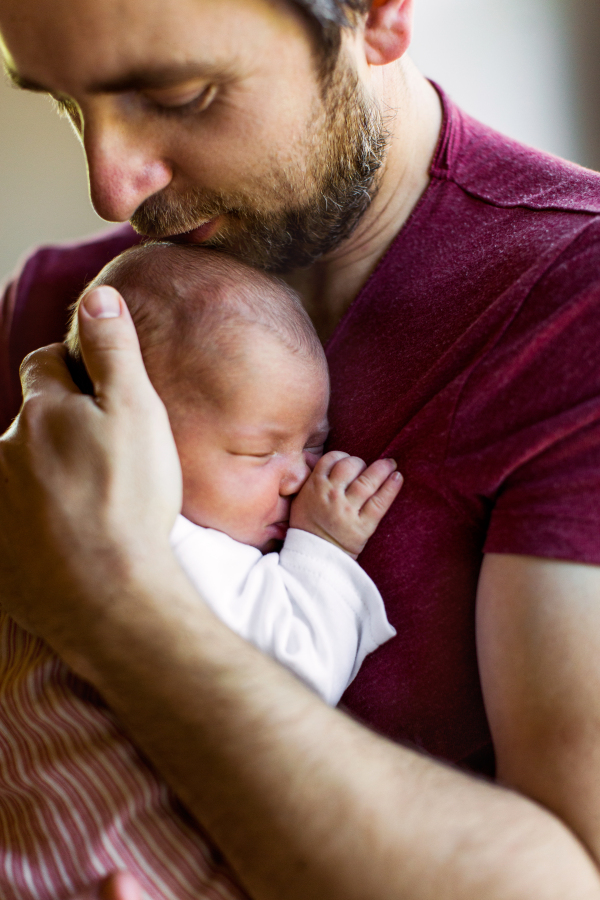 Young father at home standing at the window holding his cute newborn baby girl.