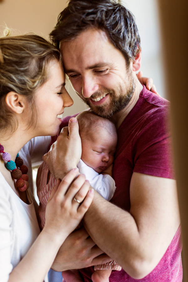 Beautiful young parents at home standing at the window holding their cute baby daughter in the arms.