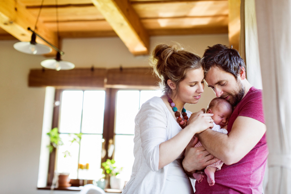 Beautiful young parents at home standing at the window holding their cute baby daughter in the arms.