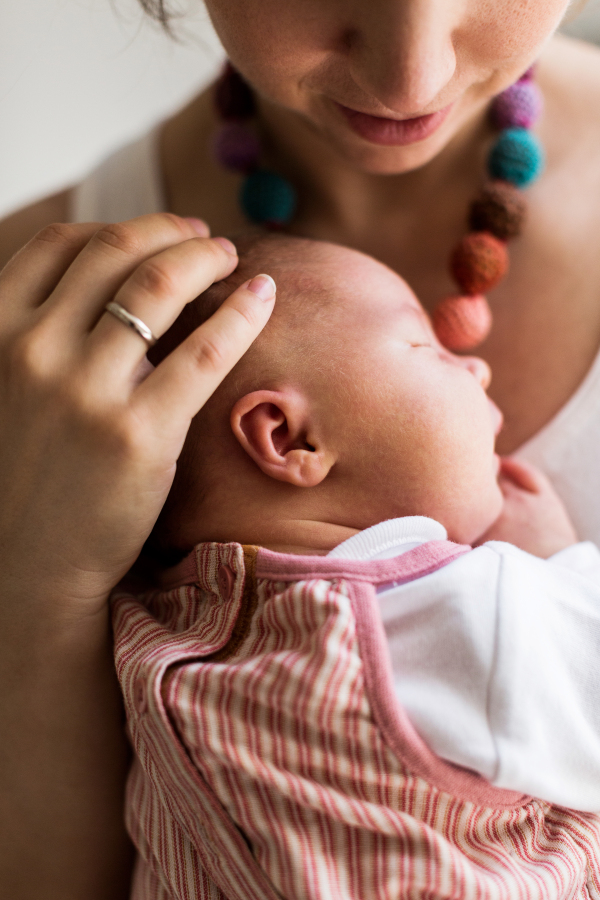 Unrecognizable young mother at home holding her cute newborn baby girl.