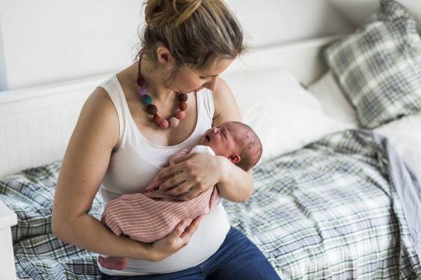 Beautiful young mother at home sitting on bed holding her cute newborn baby girl.