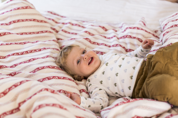 Cute little boy at home lying on bed on red striped cover, smiling.