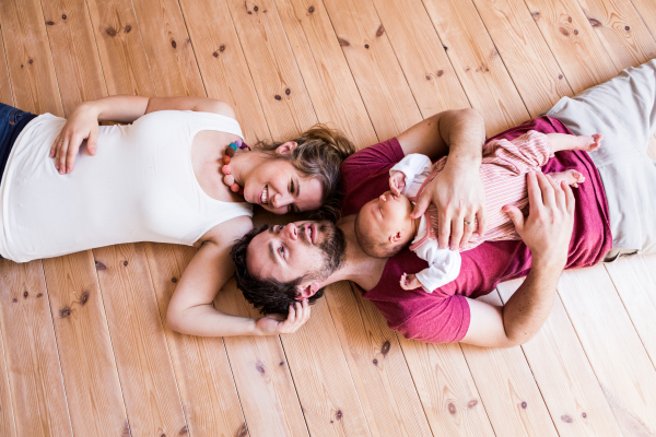 Beautiful young parents at home lying on wooden floor holding their cute baby daughter in the arms.