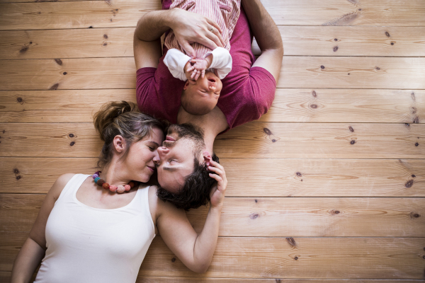 Beautiful young parents at home lying on wooden floor holding their cute baby daughter in the arms.