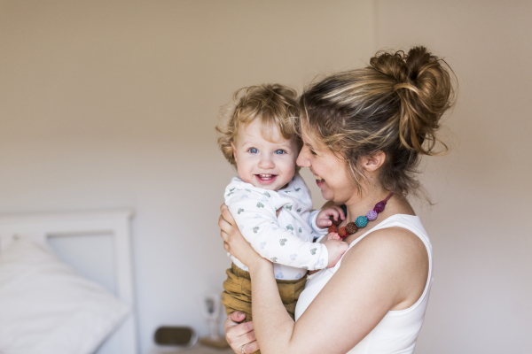 Beautiful young mother at home holding her cute little son in the arms.