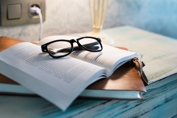 A lamp, a book and glasses on a bedside table in a hotel room.