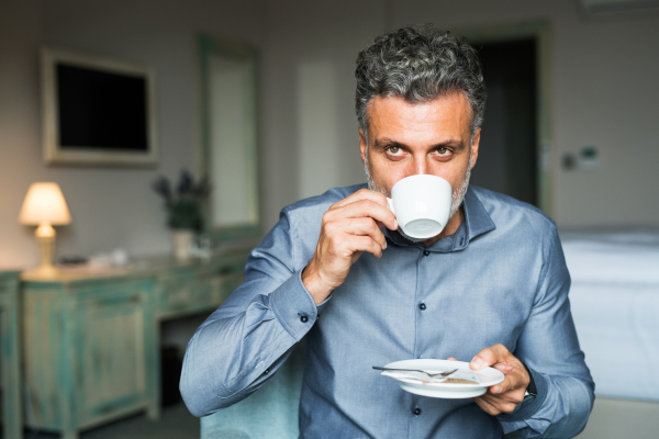 Mature, handsome businessman drinking coffee in a hotel room.