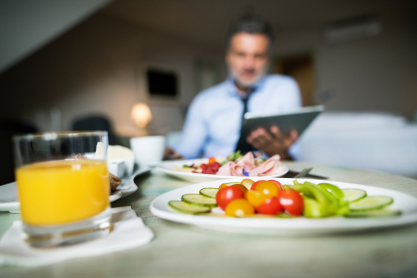 Mature, handsome businessman working on a tablet in a hotel room. A man having breakfast.