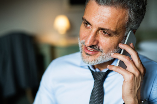 Mature businessman with smartphone in a hotel room. Handsome man making a phone call. Close up.