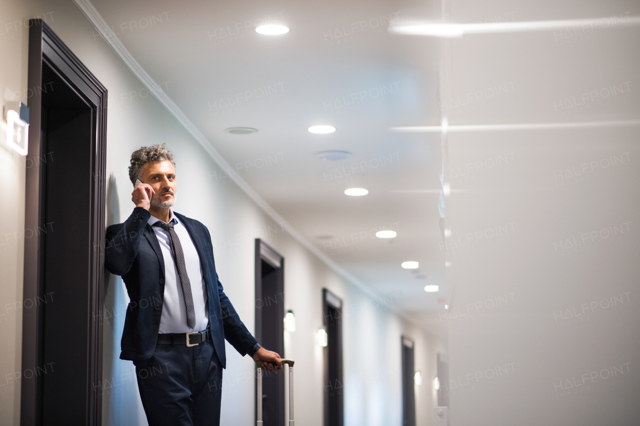 Mature businessman with smartphone in a hotel corridor. Handsome man standing in a hotel corridor, making a phone call.