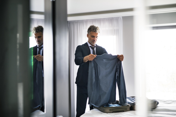 Handsome mature businessman packing his suitcase in a hotel room.