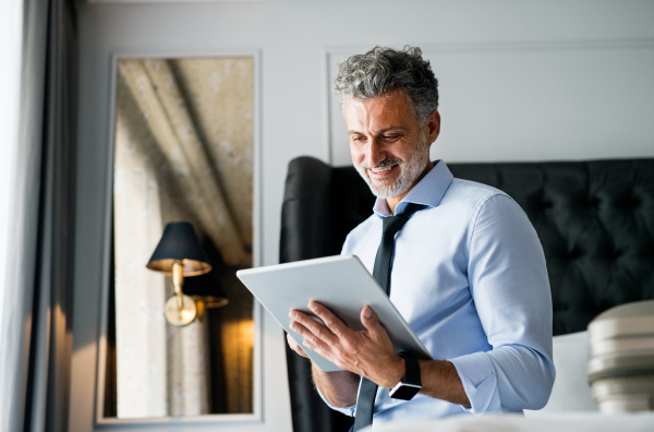 Mature, handsome businessman working on a tablet in a hotel room.