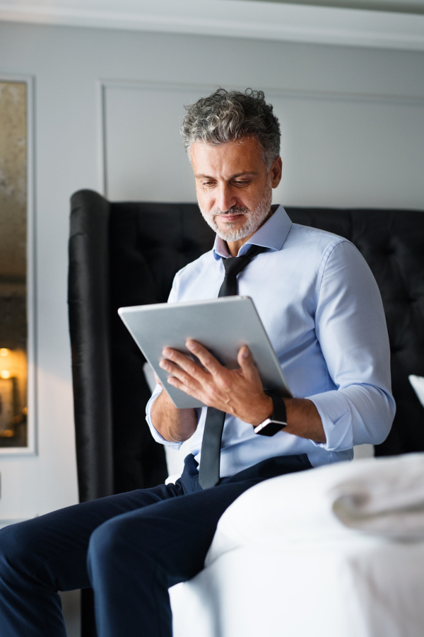 Mature, handsome businessman working on a tablet in a hotel room.