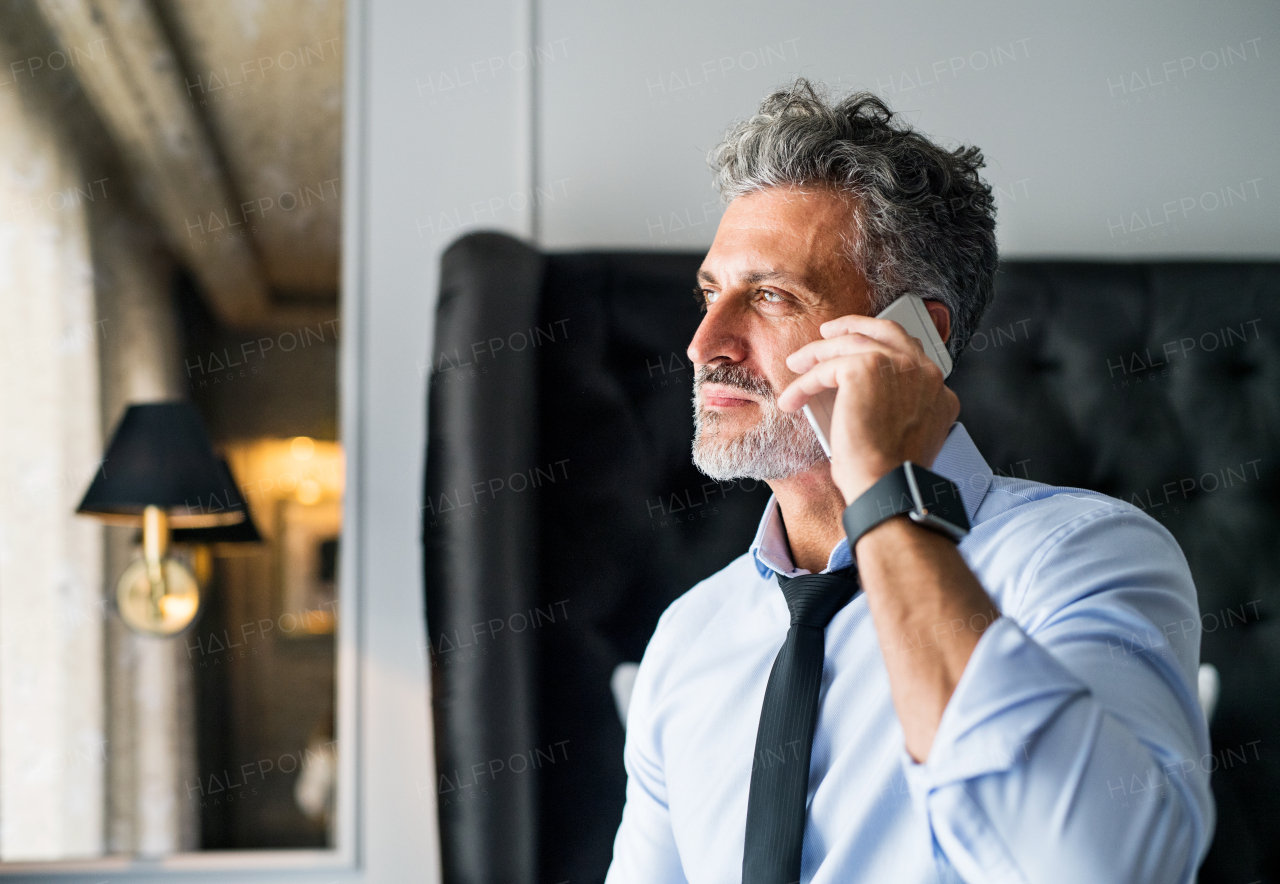 Mature businessman with smartphone in a hotel room. Handsome man making a phone call.