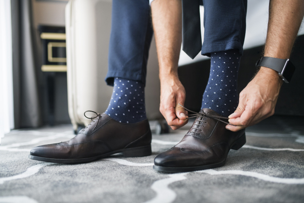 Unrecognizable businessman dressing up in a hotel room. Man tying his shoelaces. Close up.