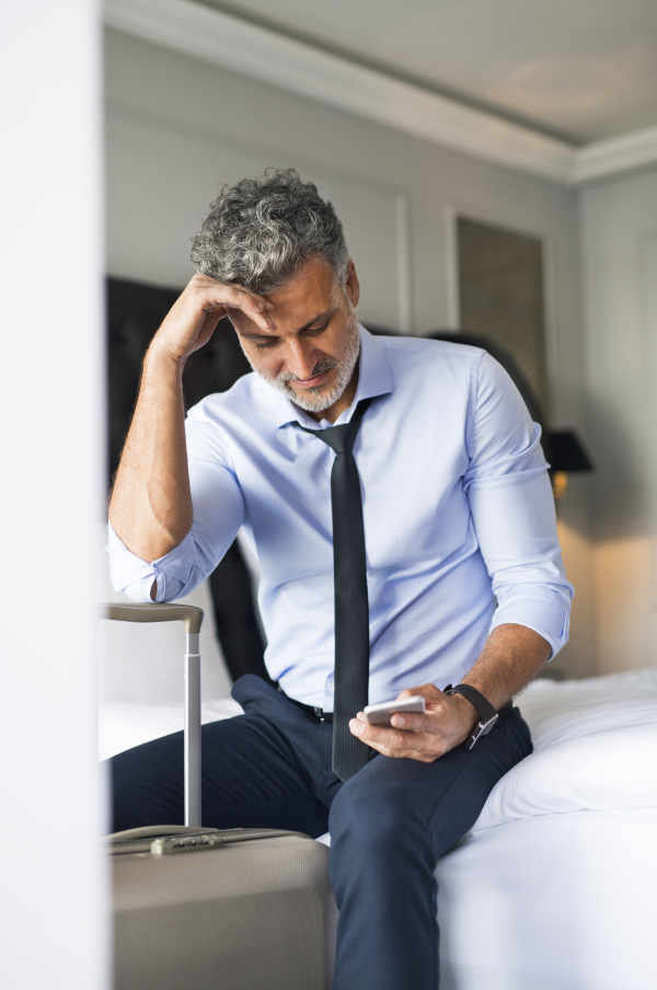 Mature businessman with a smartphone in a hotel room. Handsome man making texting.